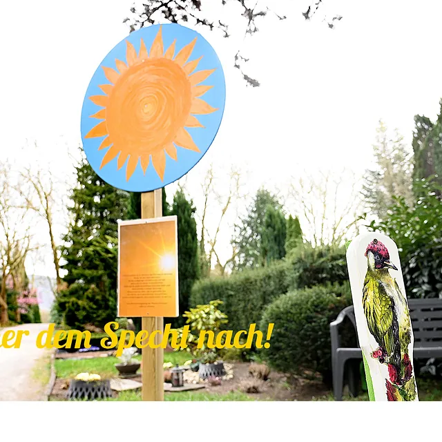 Ein Wegweiser zum Naturlehrpfad mit Sonnen- und Spechtsymbol.