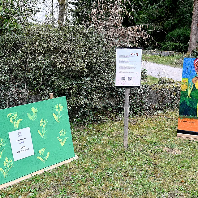 Bemalte Tafeln auf einem Lehrpfad, darunter "Gott als Gärtner".